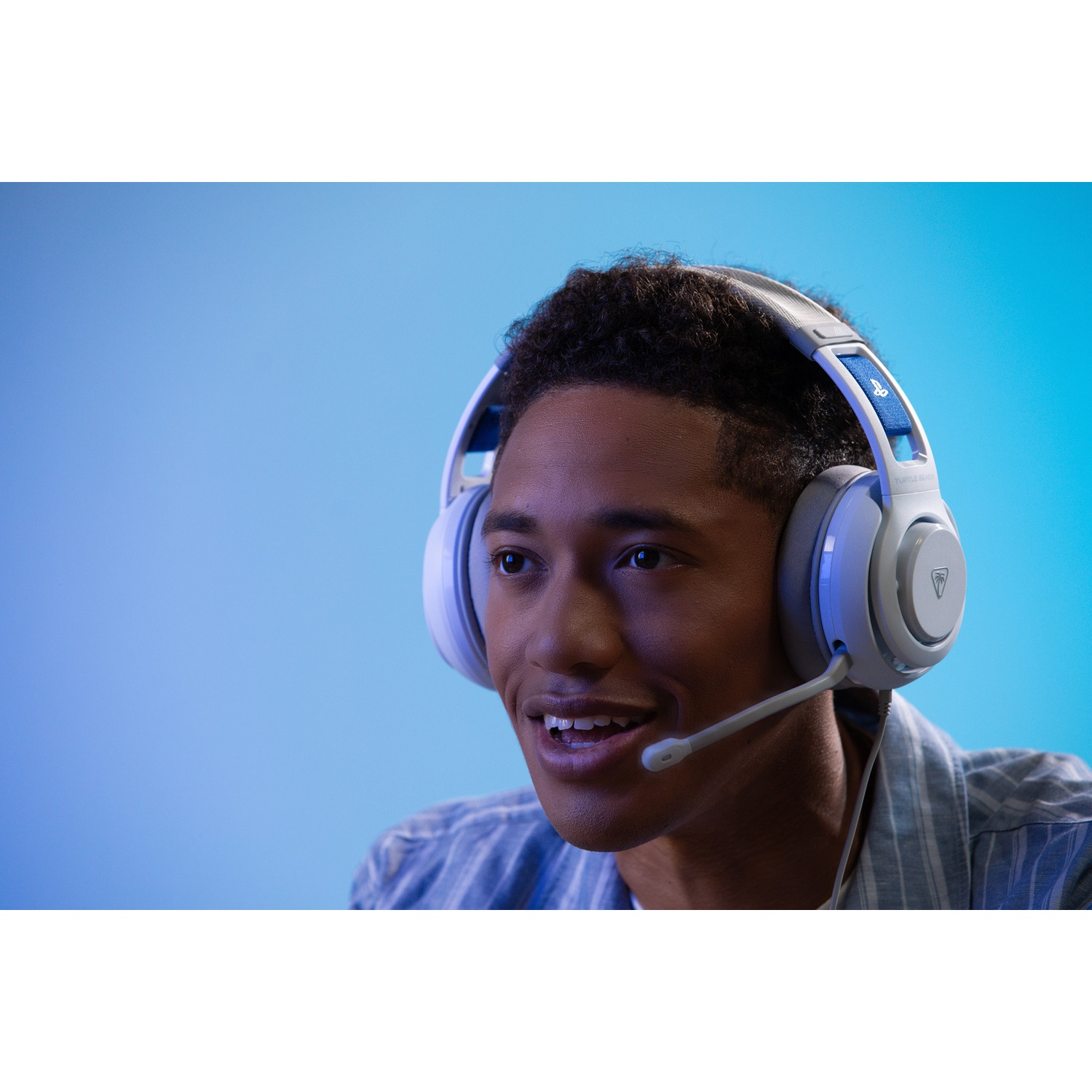A young man wearing white headphones with a microphone, smiling, against a blue gradient background.