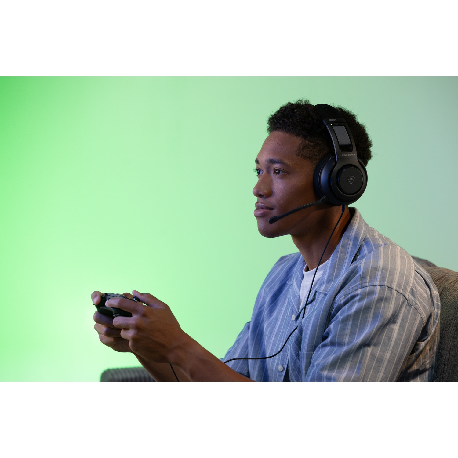 A young man wearing a headset and playing a game with a controller. The background is a gradient of green.