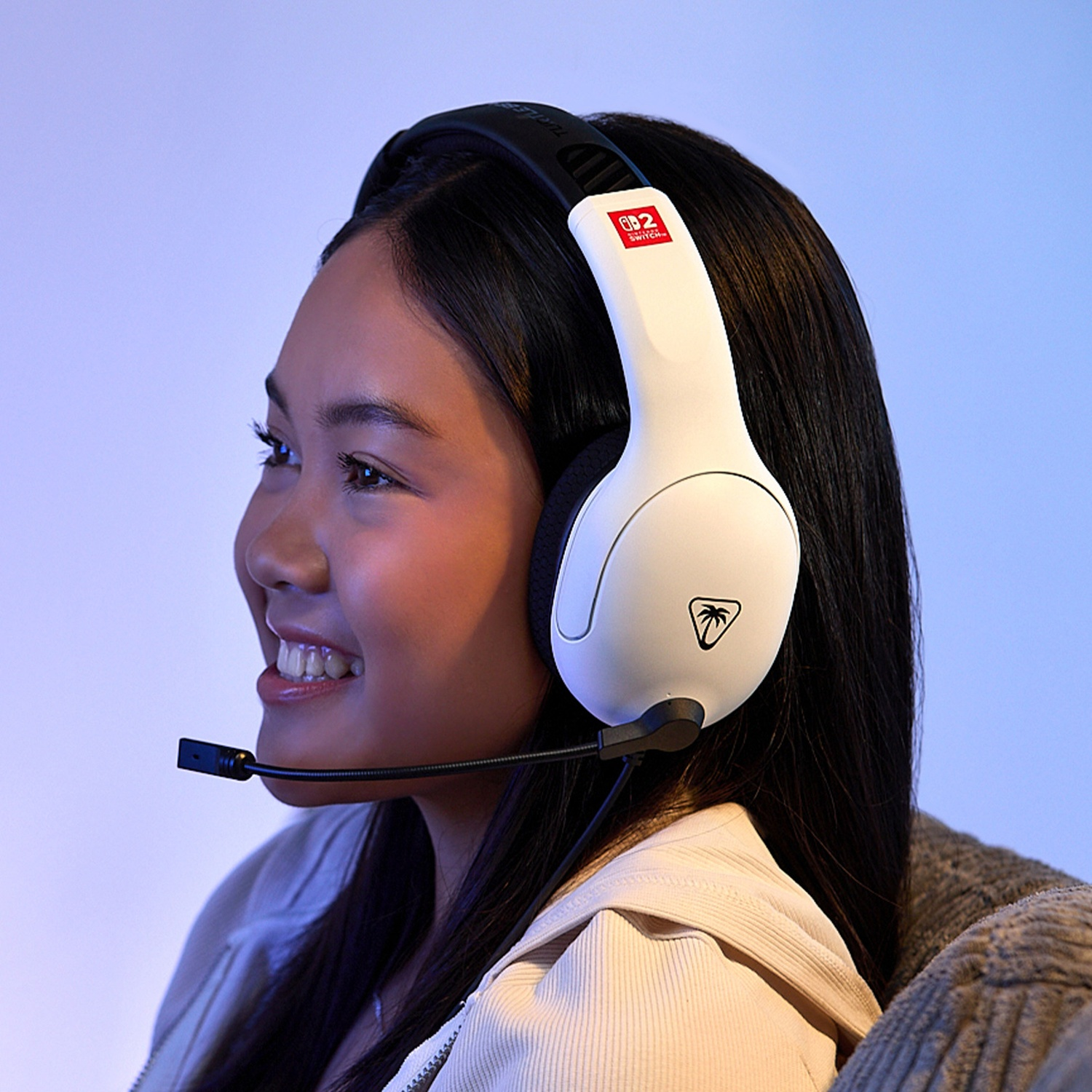 A young woman wearing white gaming headset with a microphone, smiling, with a blue gradient background.
