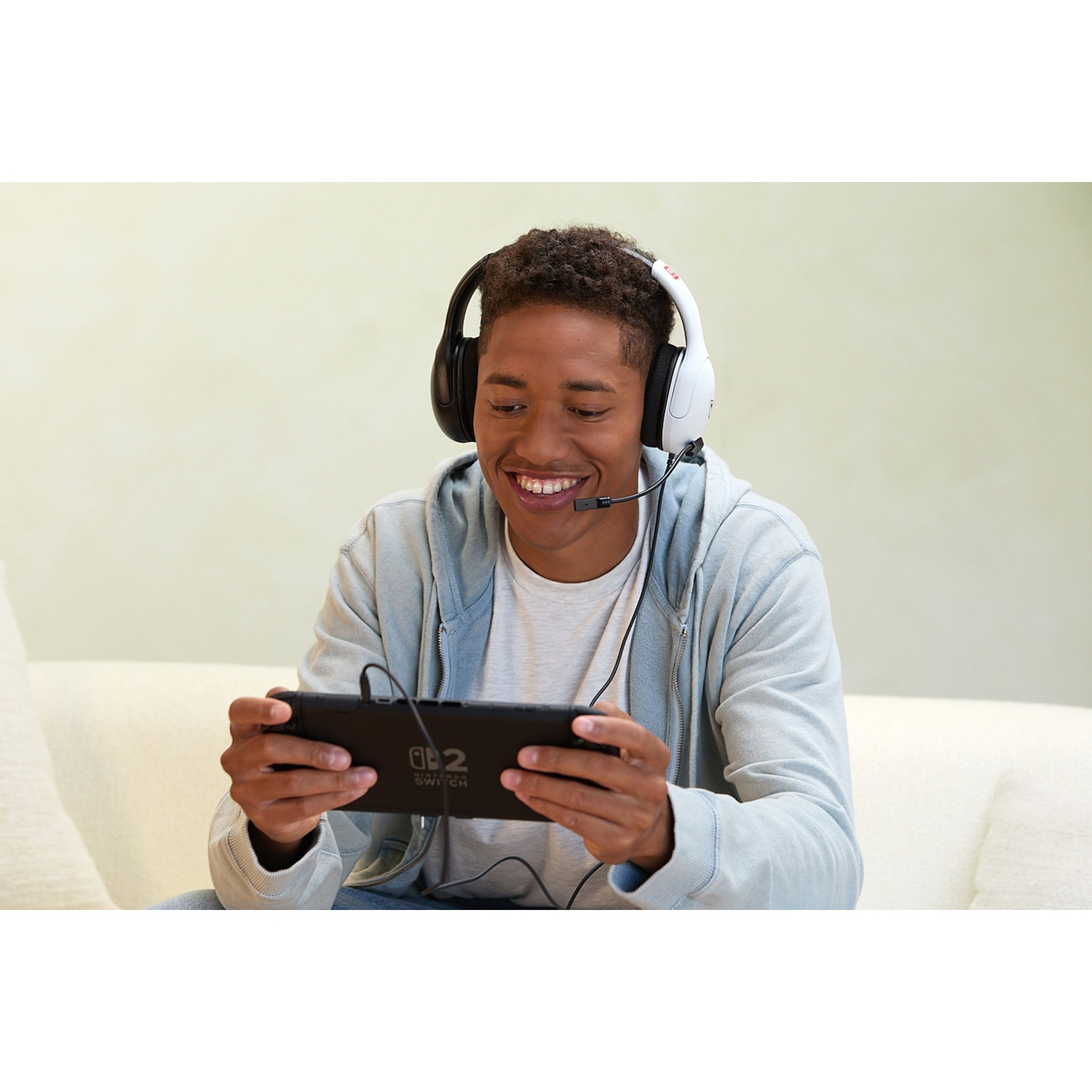 A young man with headphones is playing a Nintendo Switch. He is smiling while holding the device.