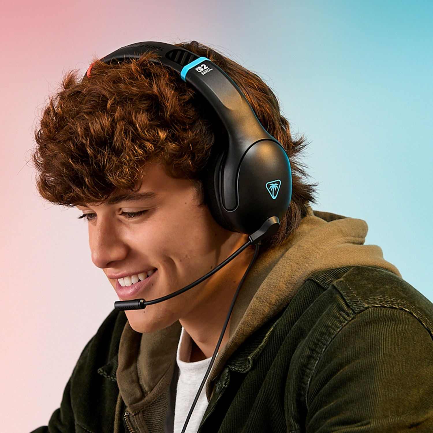 A smiling young man wearing a black headset with a microphone. He wears a green jacket and a white shirt. The background is a gradient.