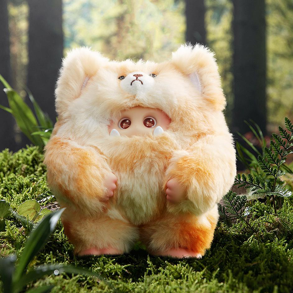 Ein Plüschtier in einer Waldumgebung. Es hat ein bärenartiges Aussehen, mit einem Puppengesicht, das herausragt. Das Spielzeug befindet sich auf einer moosigen Oberfläche.