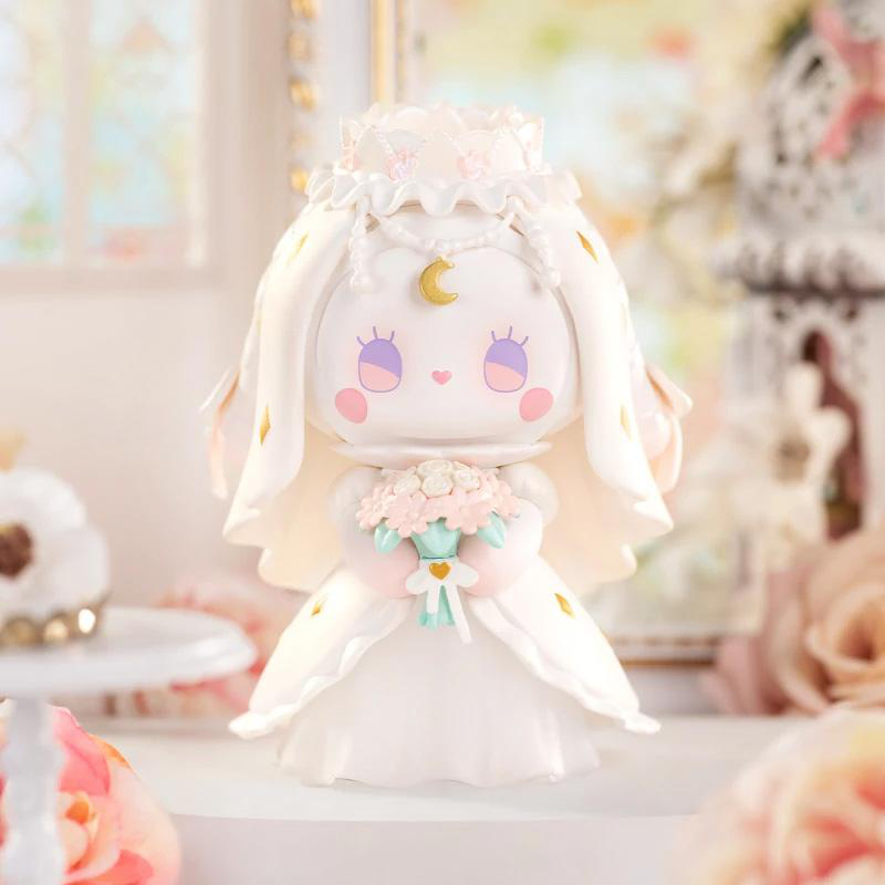 Eine weiße Brautfigur mit Krone und Schleier hält einen Blumenstrauß. Sie hat rosige Wangen, lila Augen und einen goldenen Mondanhänger.
