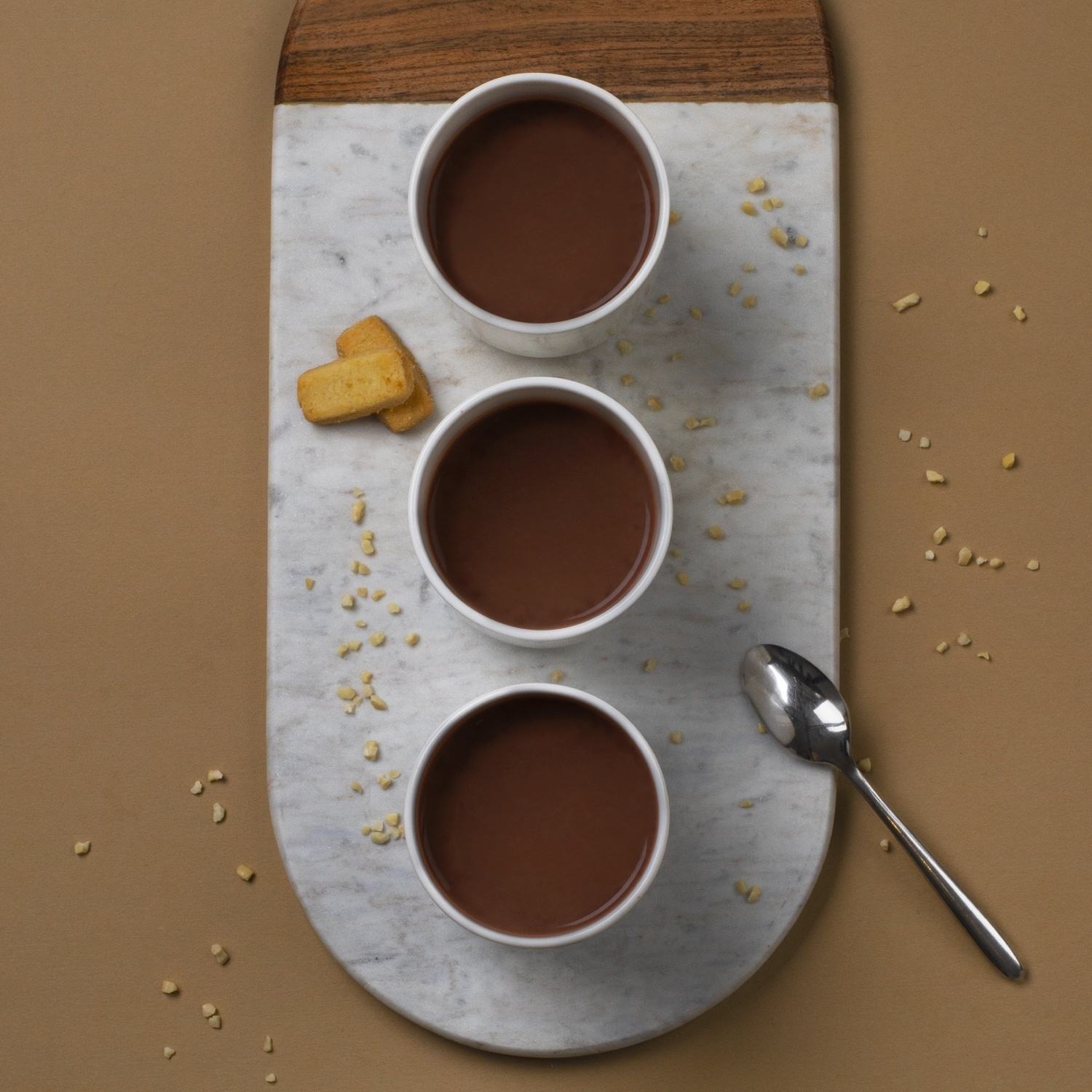 Tre tazze di cioccolata calda su una tavola di marmo con un cucchiaio. Biscotti e noci sparsi.