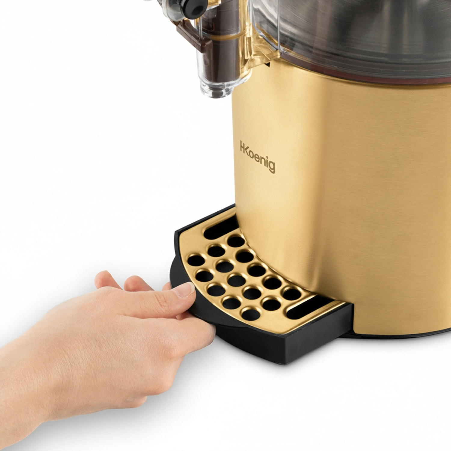 Una mano estrae un vassoio nero e oro da una macchina da caffè dorata. La macchina ha il marchio 'H Koenig'.