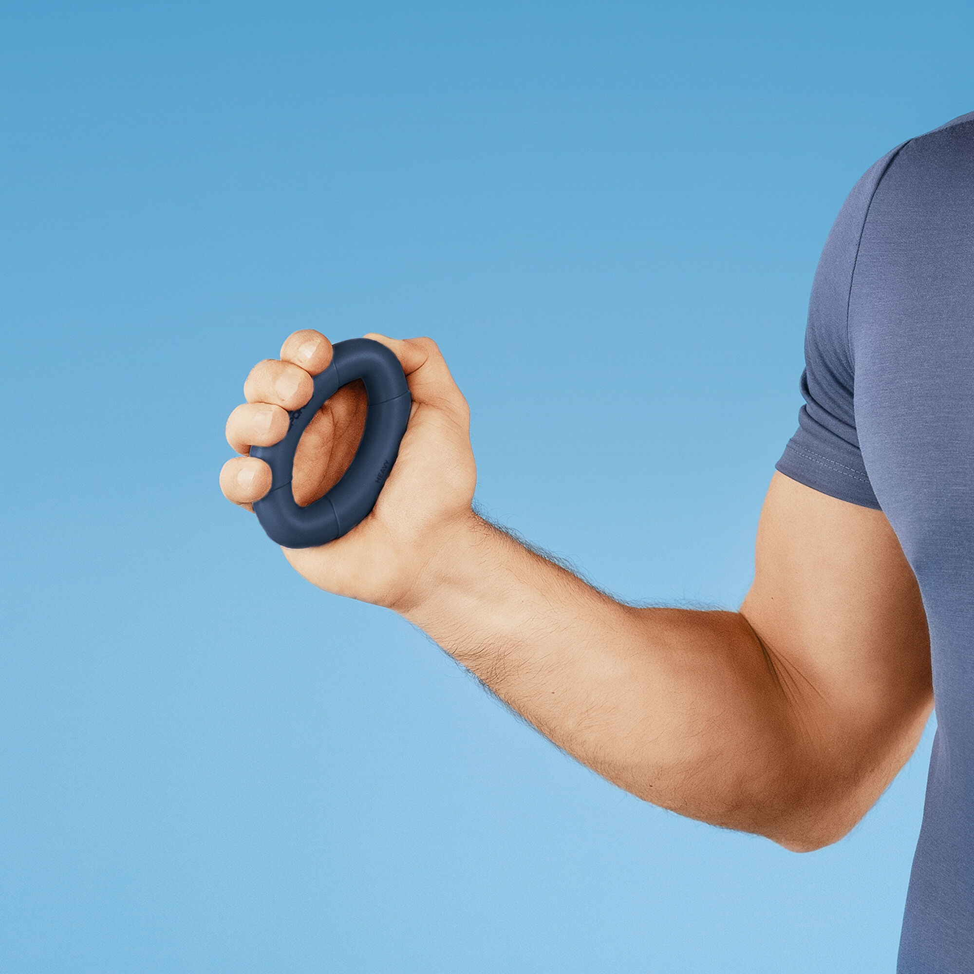 Dłoń trzyma ciemnoniebieski pierścień do wzmacniania chwytu na jasnoniebieskim tle. Osoba ma na sobie niebieską koszulę.