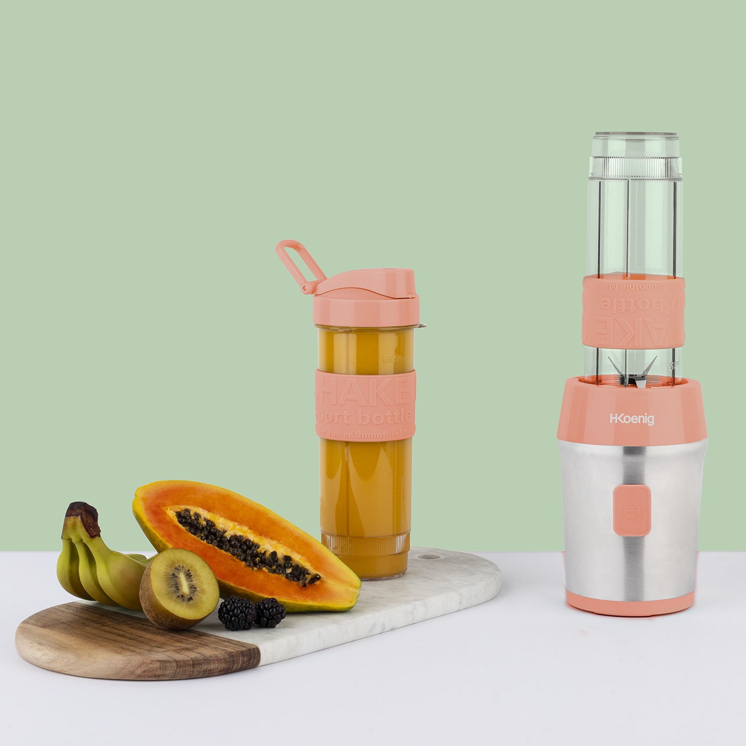 Un frullatore e una bottiglia di frullato su una superficie bianca con frutta. Include banane, papaya, kiwi e more.