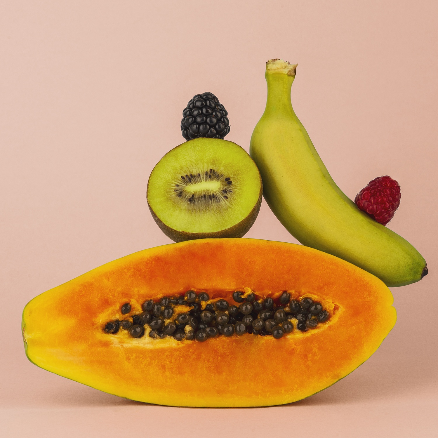 Una papaya, kiwi, banana, lampone e mora su sfondo rosa. La papaya è tagliata, mostrando semi neri.