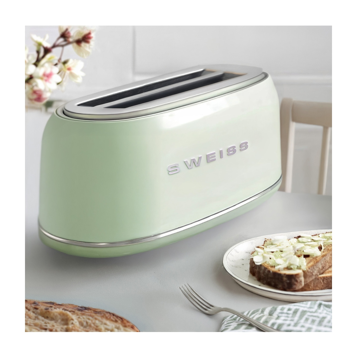 Un tostapane verde menta con la scritta 'SWISS', toast con condimenti, forchetta e fiori su un tavolo.