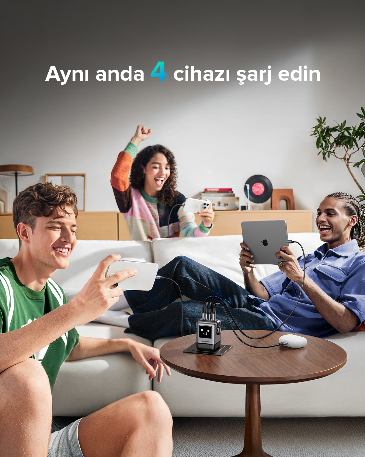 Üç kişi cihaz kullanırken, bir şarj istasyonu masanın üzerinde duruyor. Metin diyor ki: Aynı anda 4 cihazı şarj edin.