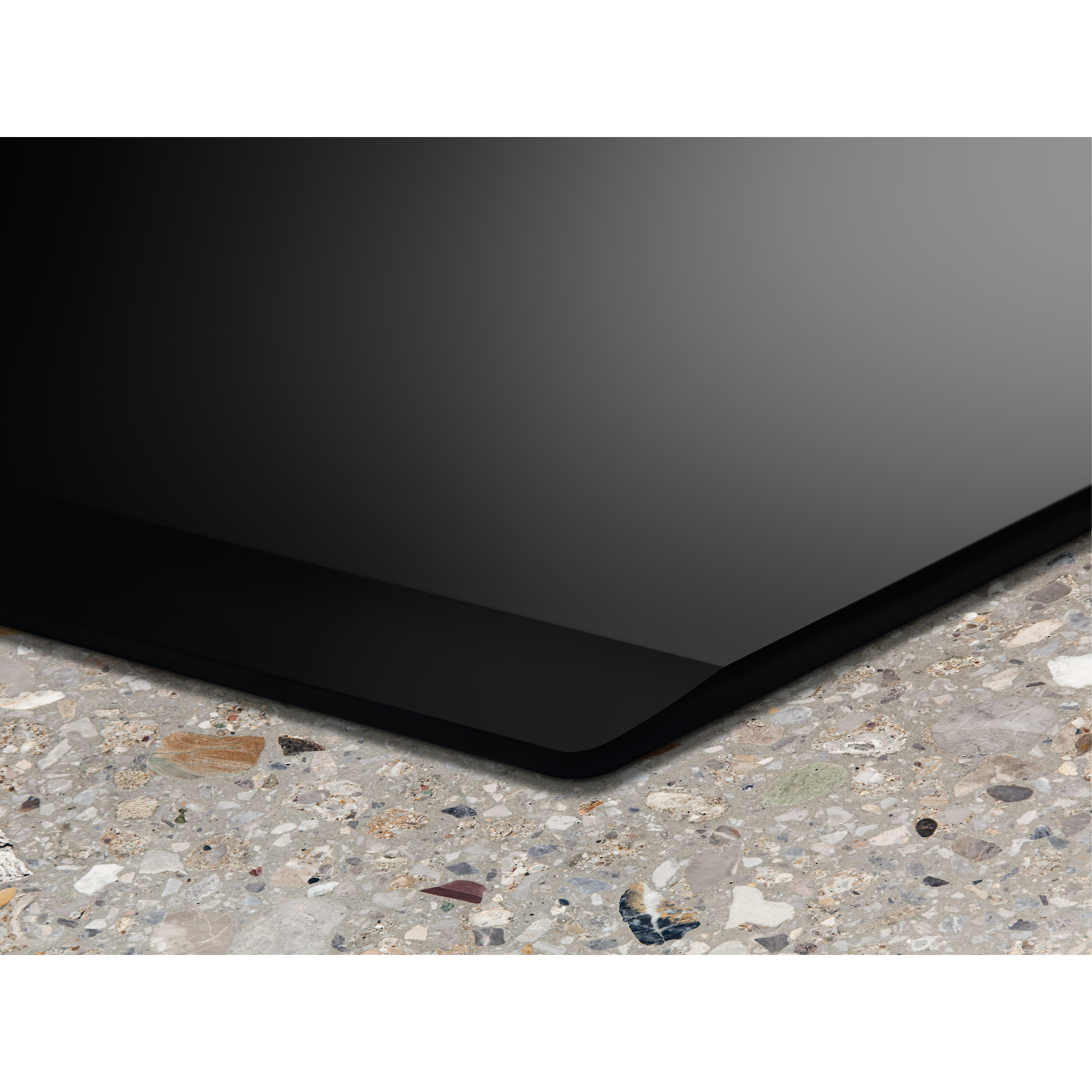 Czarny narożnik powierzchni, odbijający światło, spoczywa na nakrapianej, szarej kamiennej powierzchni.