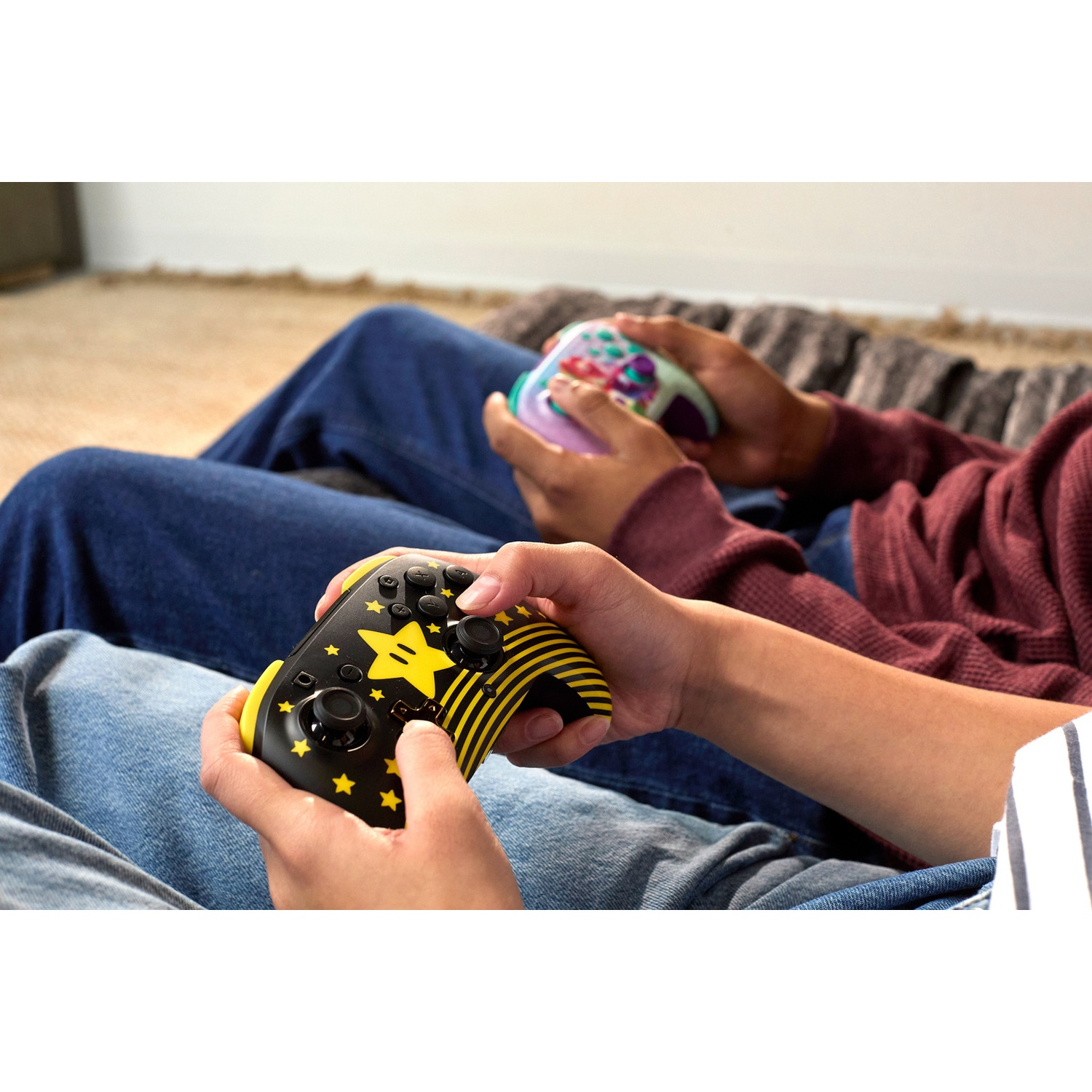 Deux personnes tiennent des manettes de jeu. Une manette est noire et jaune avec un motif d'étoile. L'autre est multicolore.