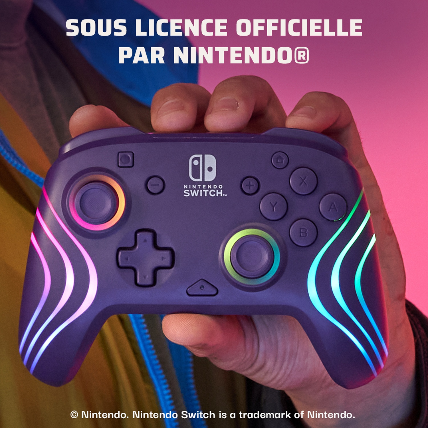 A purple Nintendo Switch controller is held in hand. It has colorful lights and buttons. The background is blurred with text at the top.