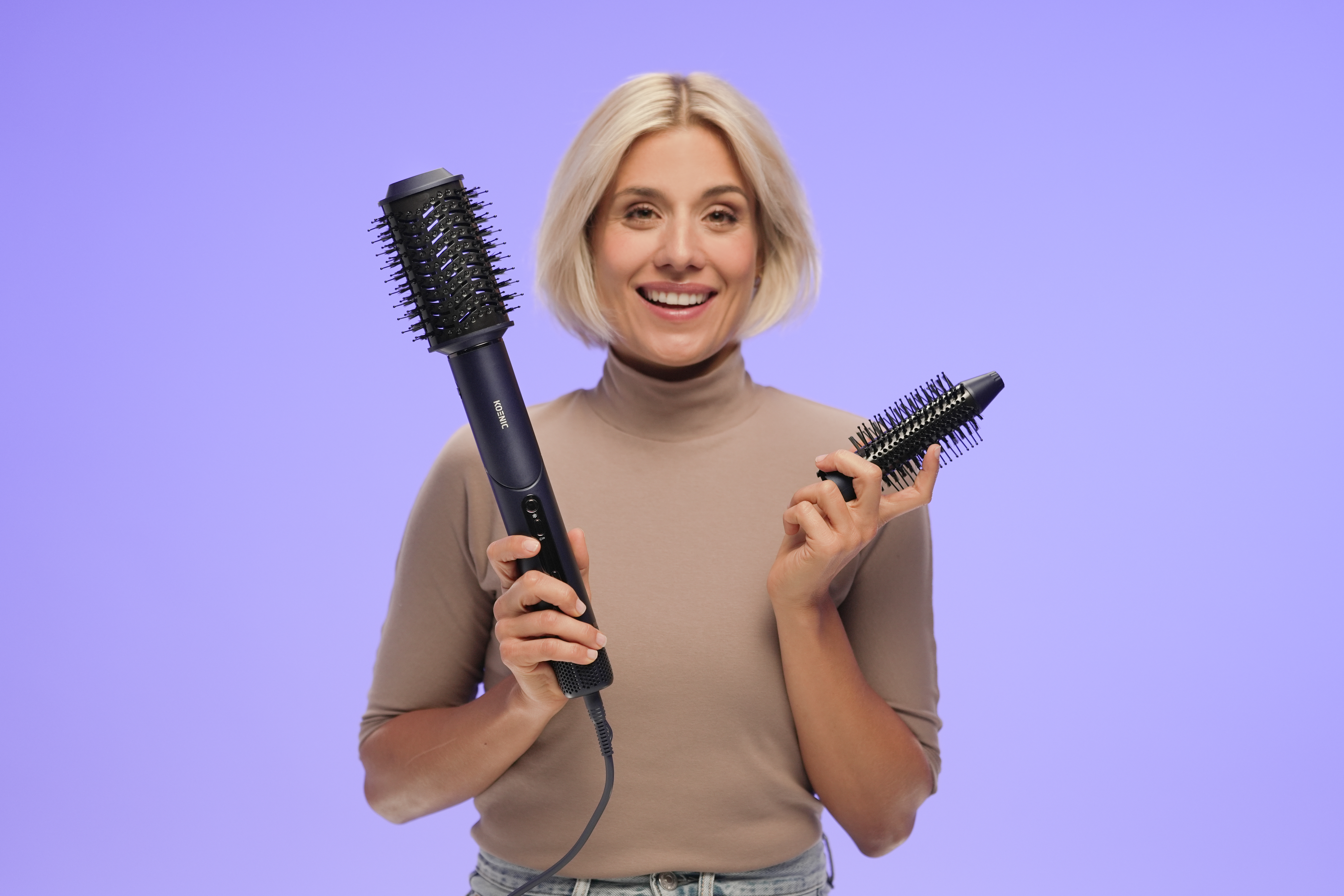 Blonde Frau hält zwei schwarze Haarstylingbürsten und lächelt in die Kamera. Lila Hintergrund.