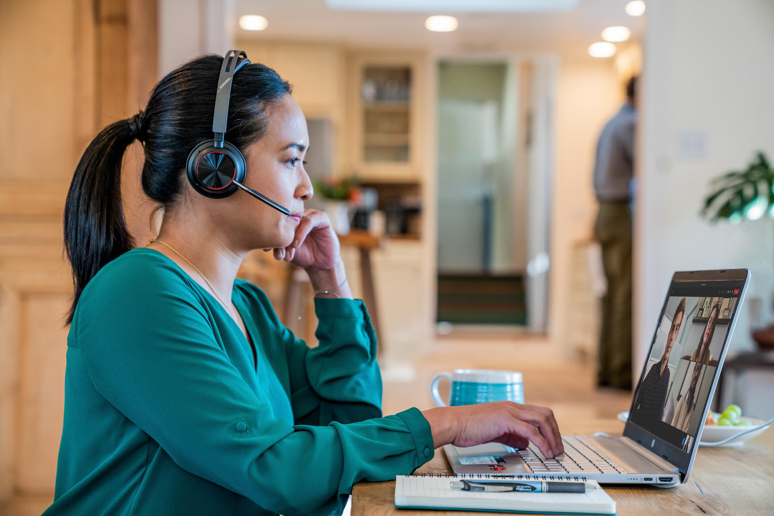 Frau mit Headset, nimmt an einem Videoanruf auf ihrem Laptop in einem Homeoffice teil.