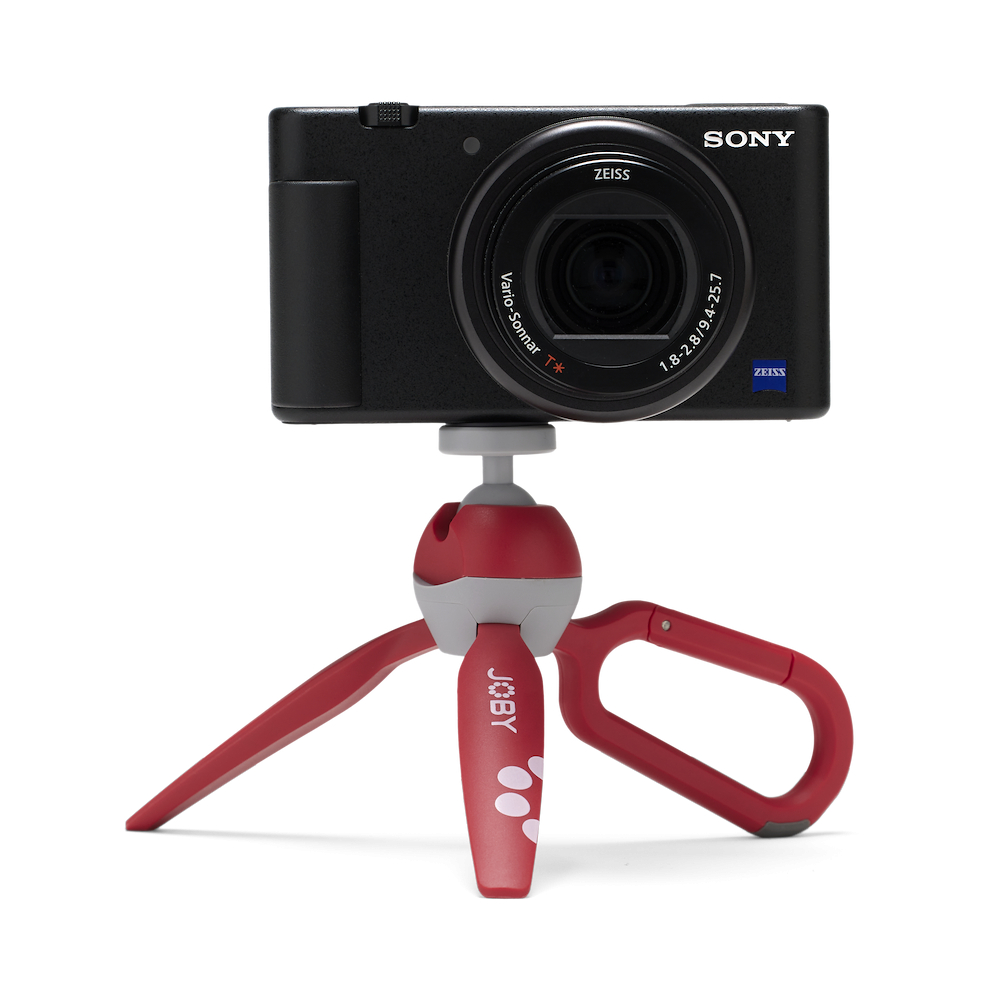 Eine schwarze Sony-Kamera auf einem rot-grauen Joby-Stativ. Die Kamera hat ein Zeiss-Objektiv. Der Hintergrund ist weiß.