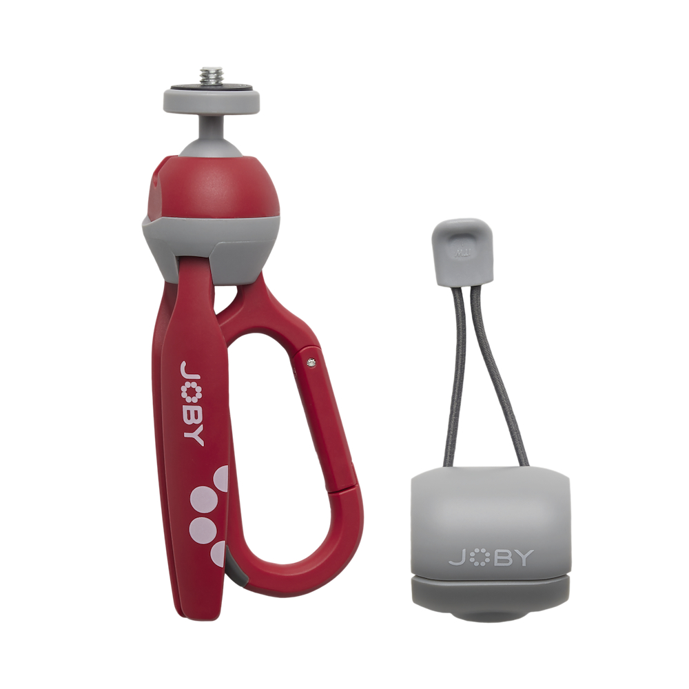 Ein rotes und graues Joby Mini-Stativ und ein graues Zubehörteil mit zwei Kabeln. Das Stativ hat einen Karabinergriff und einen Kugelkopf.