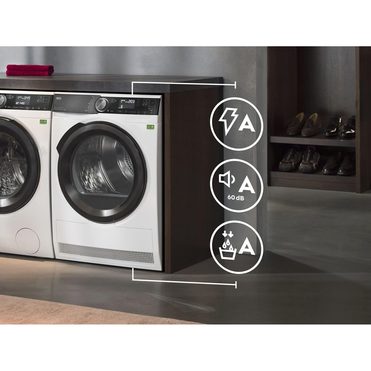 White washing machines with black details. Icons show energy efficiency, sound level, and water efficiency. Shoes are on a shelf in the background.