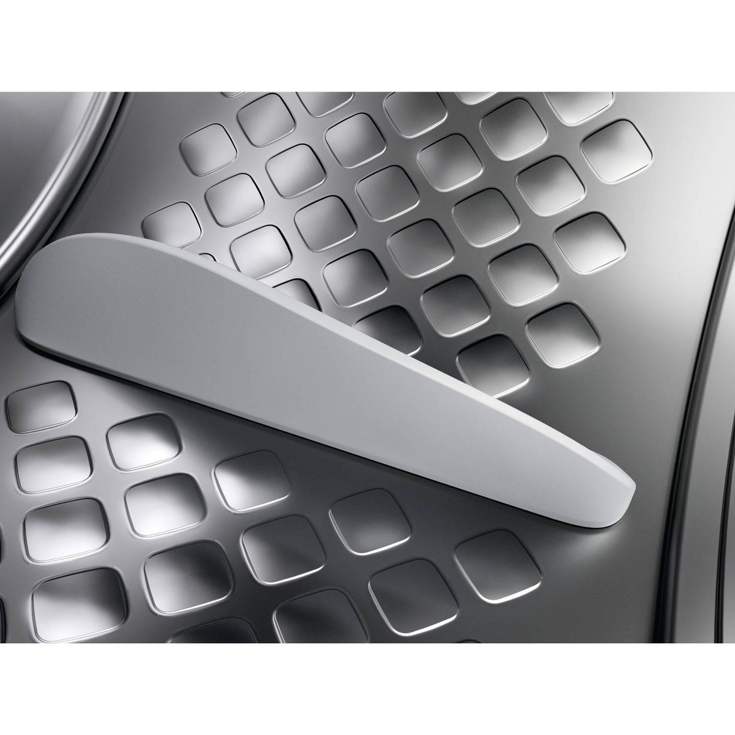 Close-up of a washing machine's interior. A gray handle lies across a textured, silver surface with square indentations.