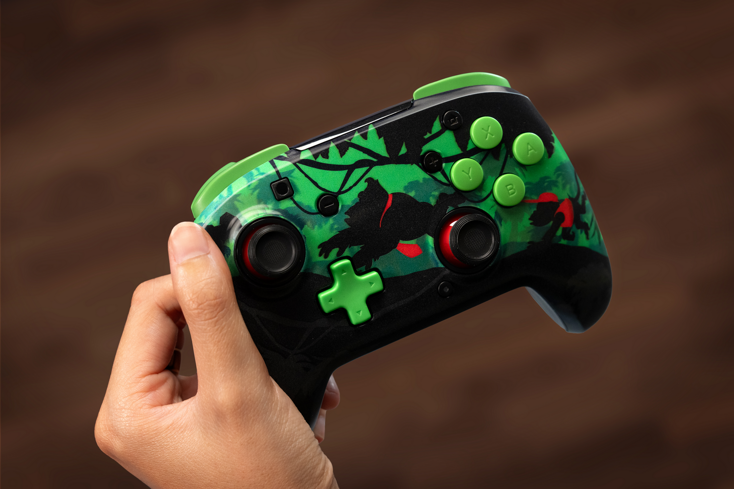 Mano sosteniendo un controlador negro y verde con un diseño de jungla. El controlador tiene botones verdes y un fondo marrón.