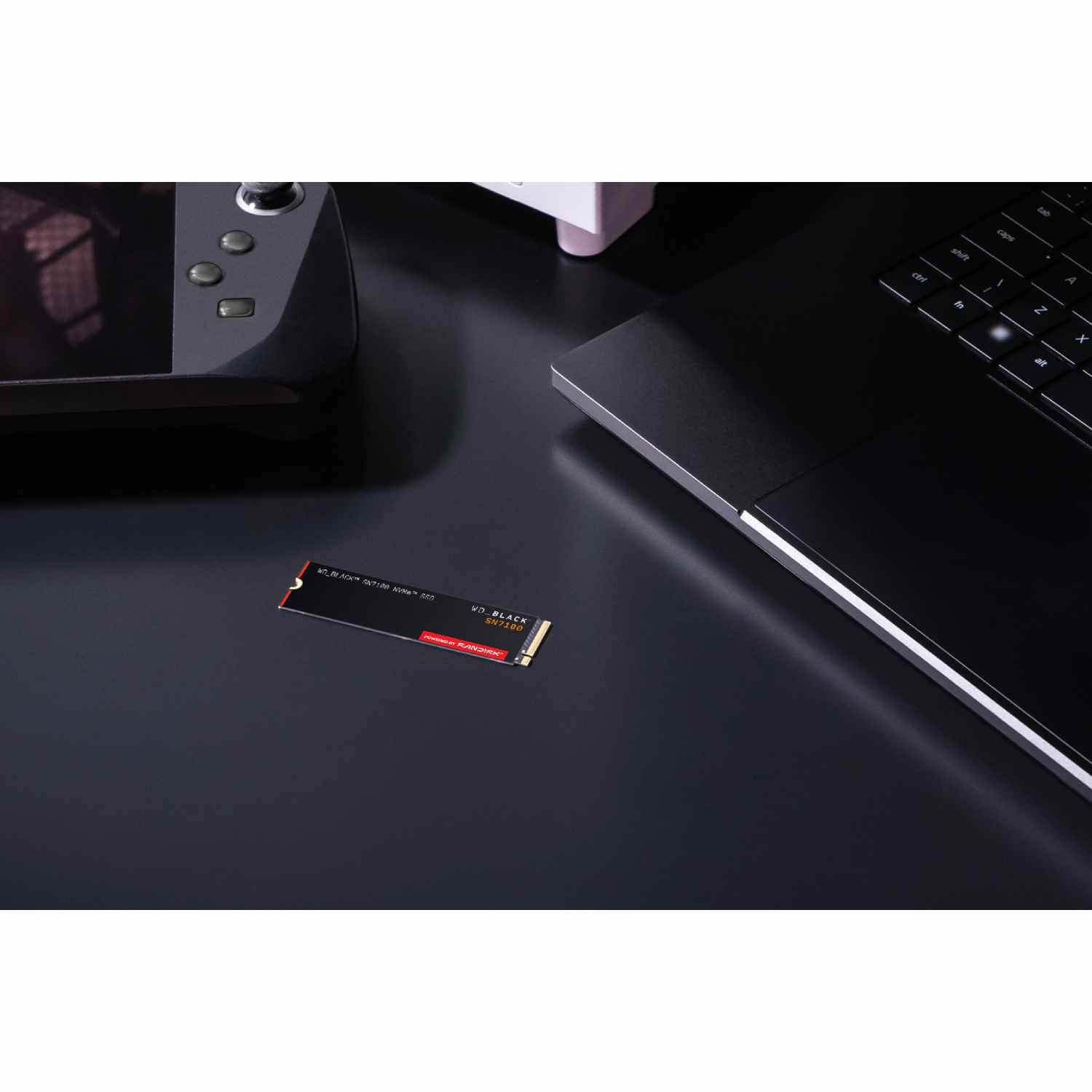 SSD negra sobre un escritorio negro, con una laptop y una consola portátil visibles. La SSD tiene texto rojo y blanco.