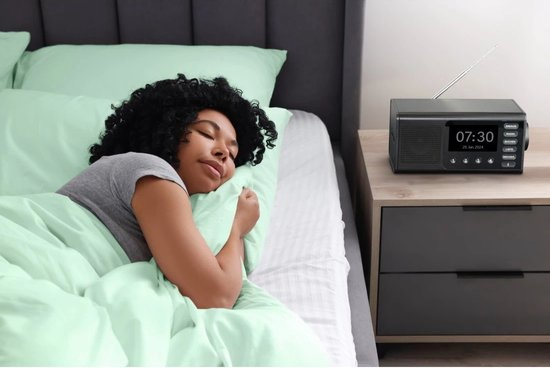 Eine Frau schläft im Bett. Ein Radio steht auf dem Nachttisch. Die Uhrzeit ist 7:30 Uhr. Die Bettwäsche ist mintgrün.