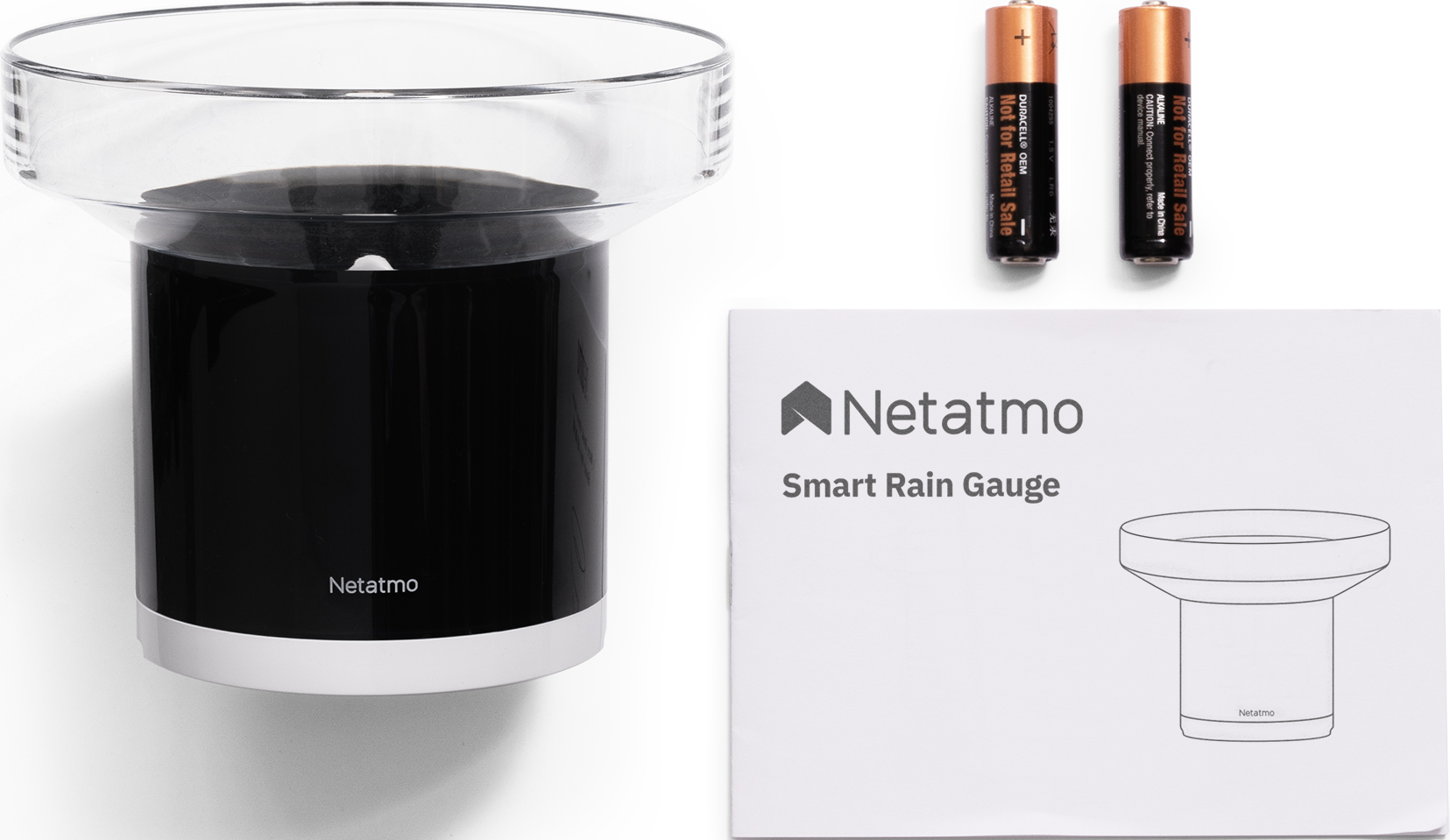 Un pluviomètre intelligent avec une base noire et un dessus transparent, des piles et un guide Netatmo sur une surface blanche.