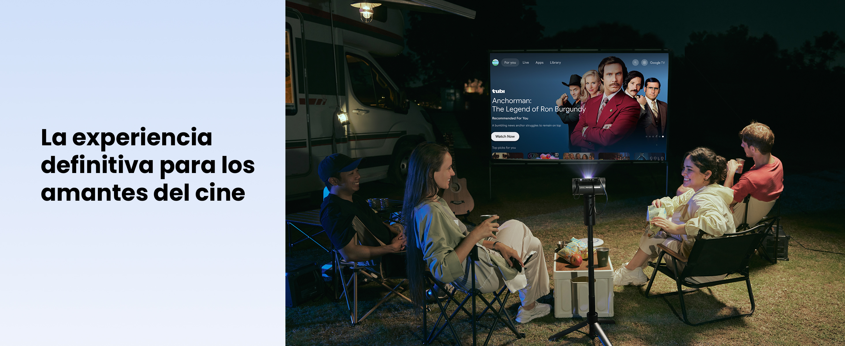 Personas viendo una película al aire libre por la noche. Una pantalla muestra 'Anchorman'. Un proyector está frente a la pantalla. Una autocaravana está detrás.