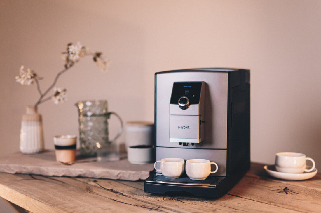 Ekspres do kawy z dwoma filiżankami. Inne przedmioty na drewnianym stole, w tym wazon z kwiatami i filiżanka kawy.