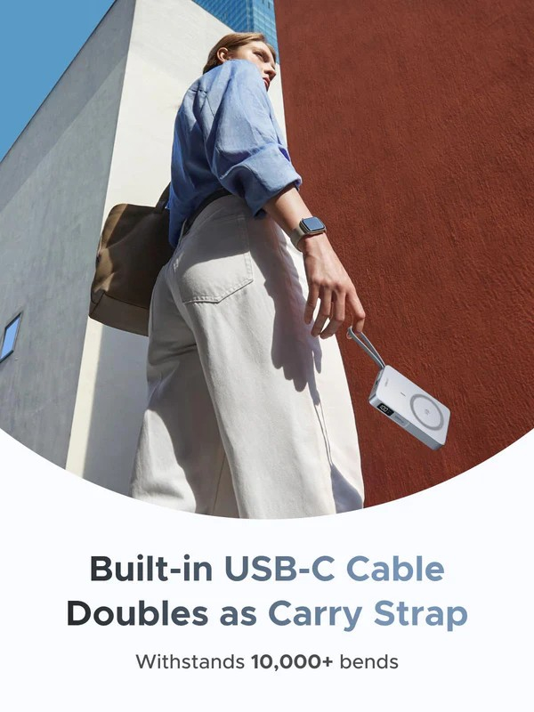 Eine Person hält eine weiße Powerbank mit eingebautem USB-C-Kabel. Die Person trägt ein blaues Hemd und weiße Hose, steht an einer roten Wand.