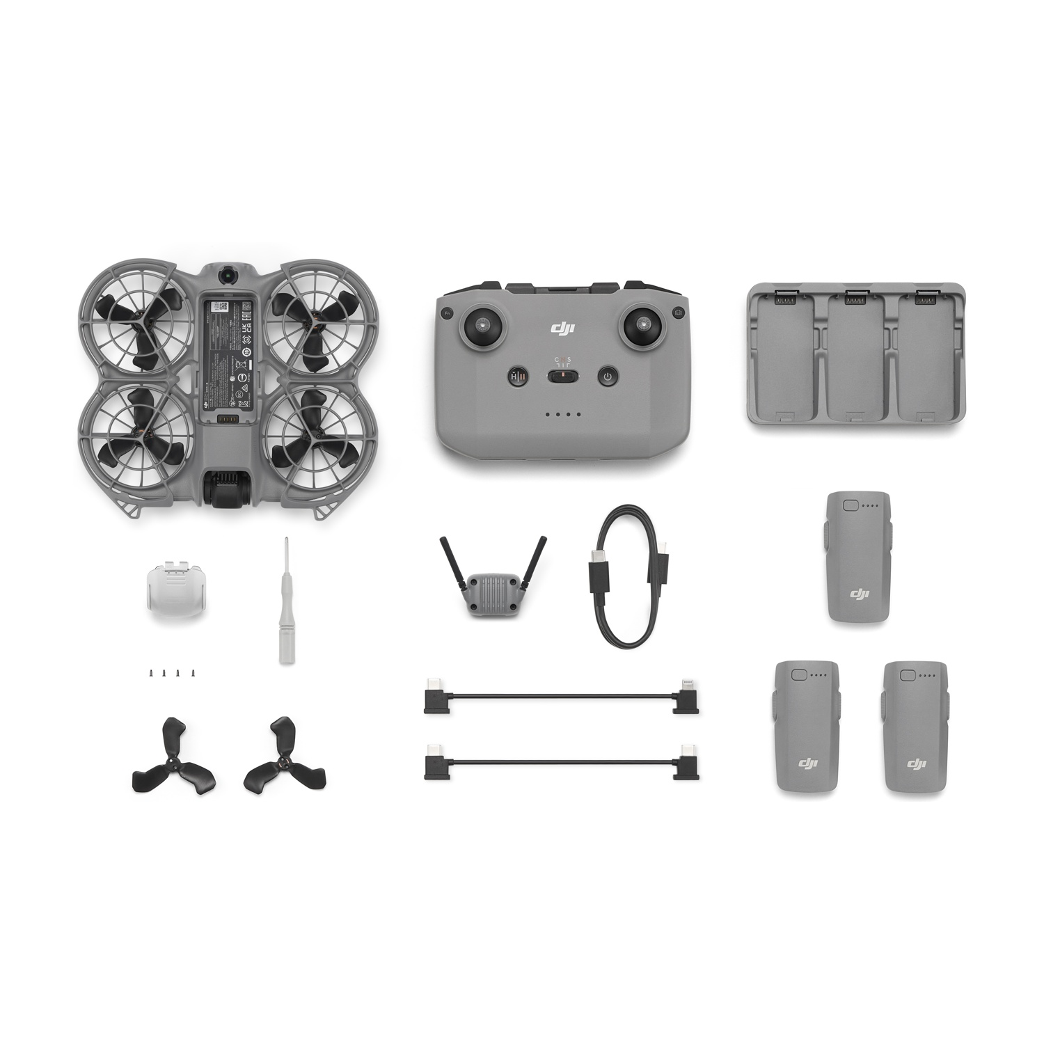 Componenti del kit drone: drone, telecomando, batterie, caricabatterie, cavi, eliche, cacciavite e altri accessori su bianco.