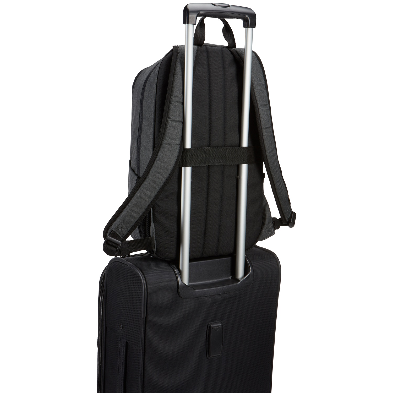 Un sac à dos noir repose sur une valise noire à roulettes. Le sac à dos est attaché à la poignée de la valise. Le fond est blanc.