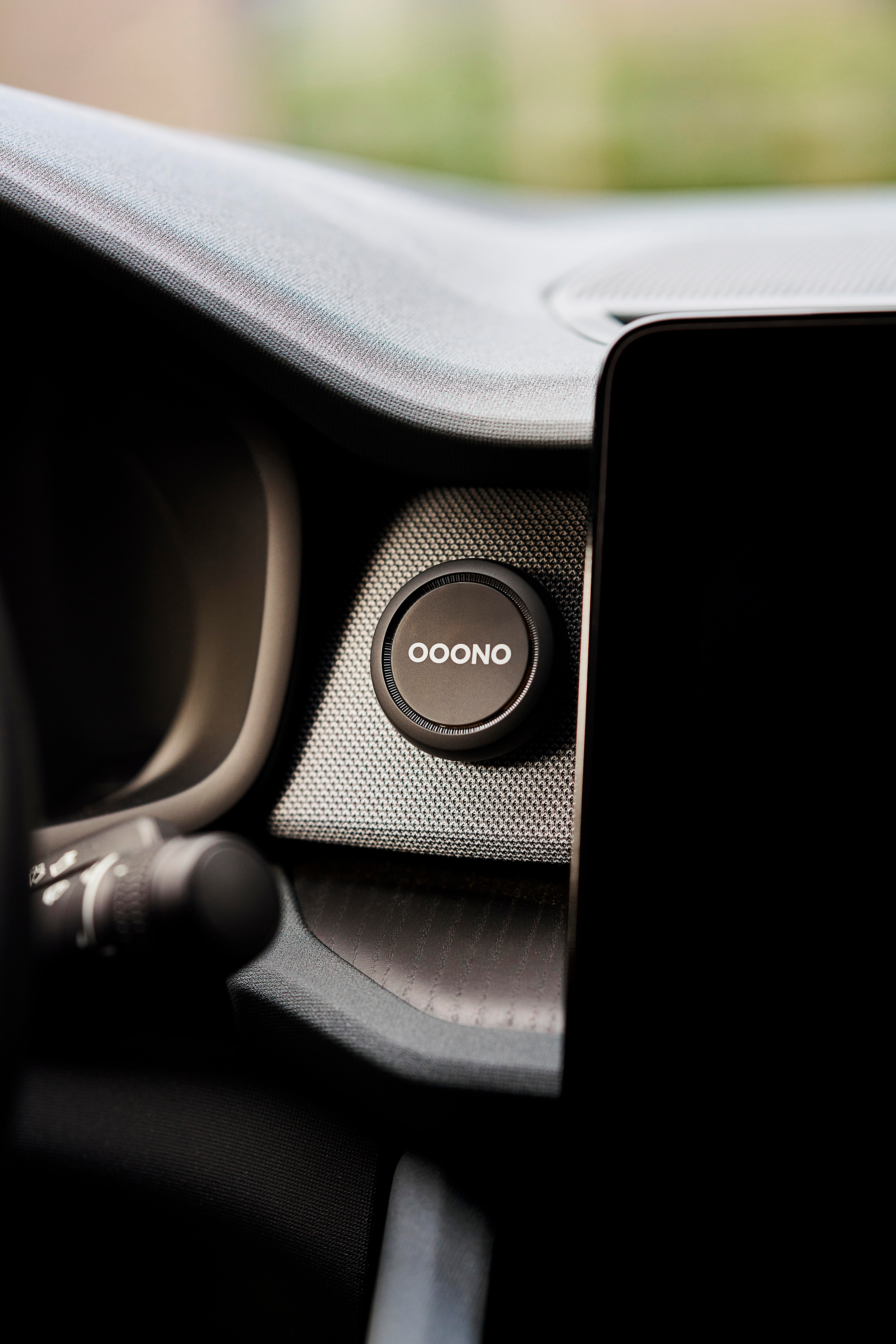 Nahaufnahme eines Armaturenbretts. Ein runder Knopf mit 'OOONO' ist zu sehen, ebenso ein schwarzer Bildschirm und Innendetails.