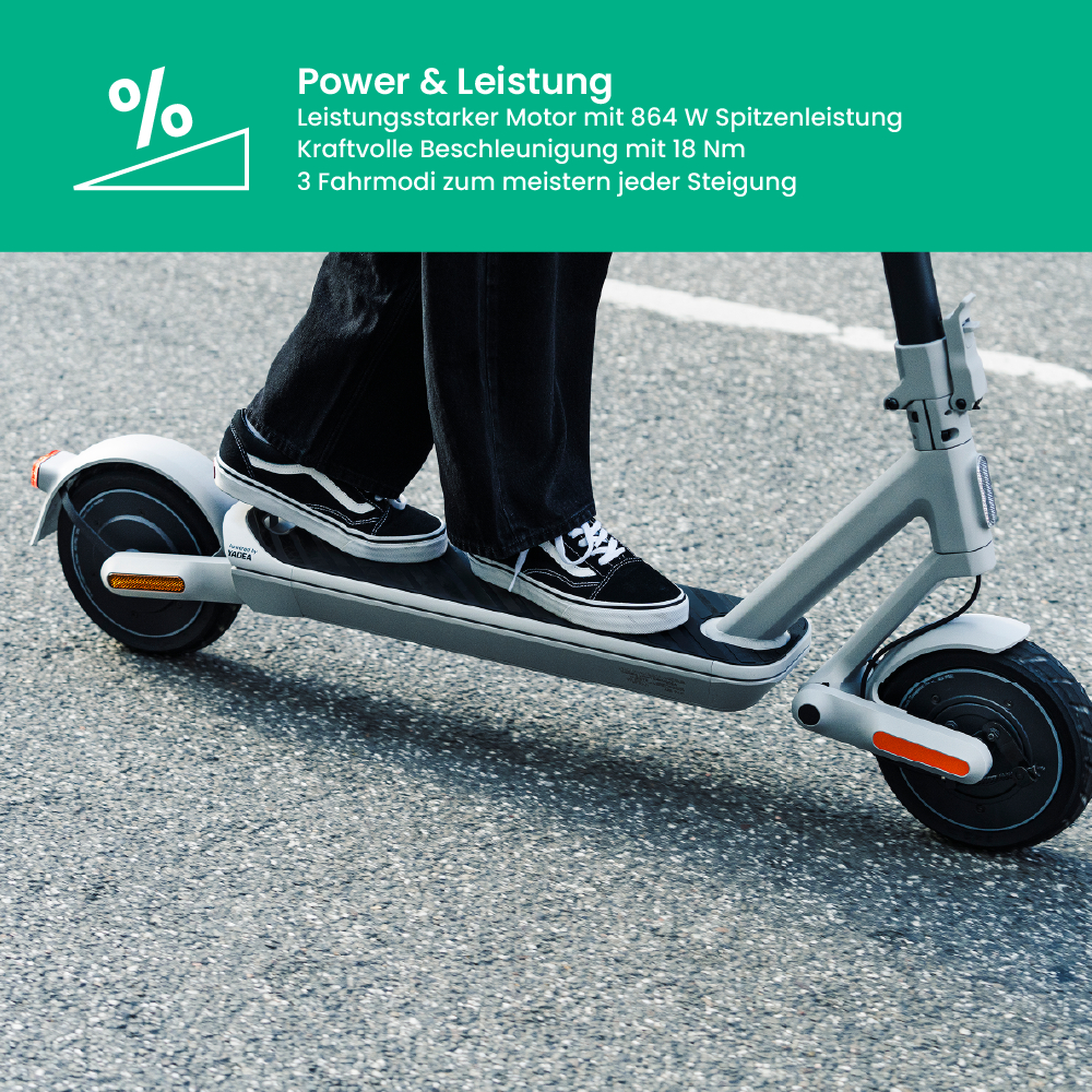 Eine Person fährt einen grauen Elektroroller auf Asphalt. Sie trägt eine schwarze Hose und Turnschuhe. Der Roller hat schwarze Räder und orangefarbene Lichter.