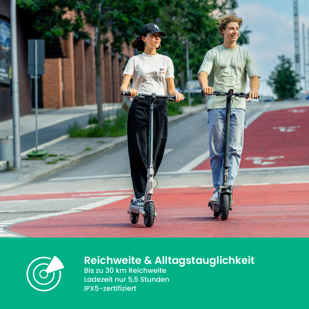 Zwei Personen fahren mit Elektrorollern auf einem roten Radweg. Einer trägt eine schwarze Kappe, der andere ein grünes Hemd. Hintergrund: Gebäude und Bäume.