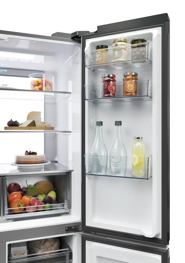 Offener Kühlschrank mit Lebensmitteln: Gläser, Flaschen, Früchte, Käse und Kuchen. Weißer Innenraum mit Glasböden und Schubladen.