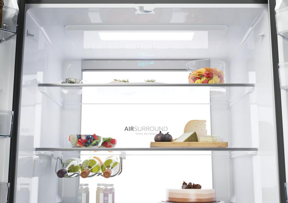 Im Kühlschrank: Obst, Käse, Nudeln, Weinflaschen und Kuchen sind auf den Regalen zu sehen. Der Kühlschrank ist weiß und sauber.
