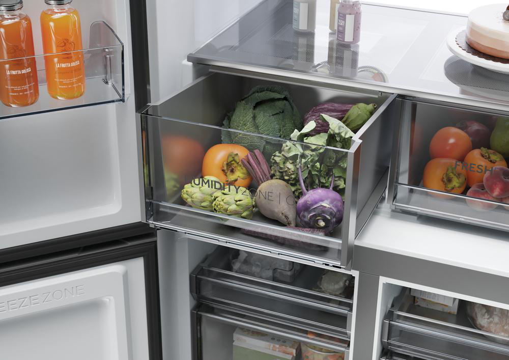 Im Kühlschrank befinden sich Obst und Gemüse in Schubladen. Saftflaschen stehen auf einem Regal. Oben ist ein Kuchen zu sehen.