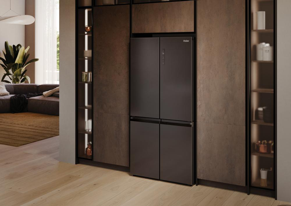 Ein schwarzer Haier-Kühlschrank steht in einer modernen Küche mit Holzboden, angrenzenden Schränken und einem Blick auf ein Wohnzimmer.
