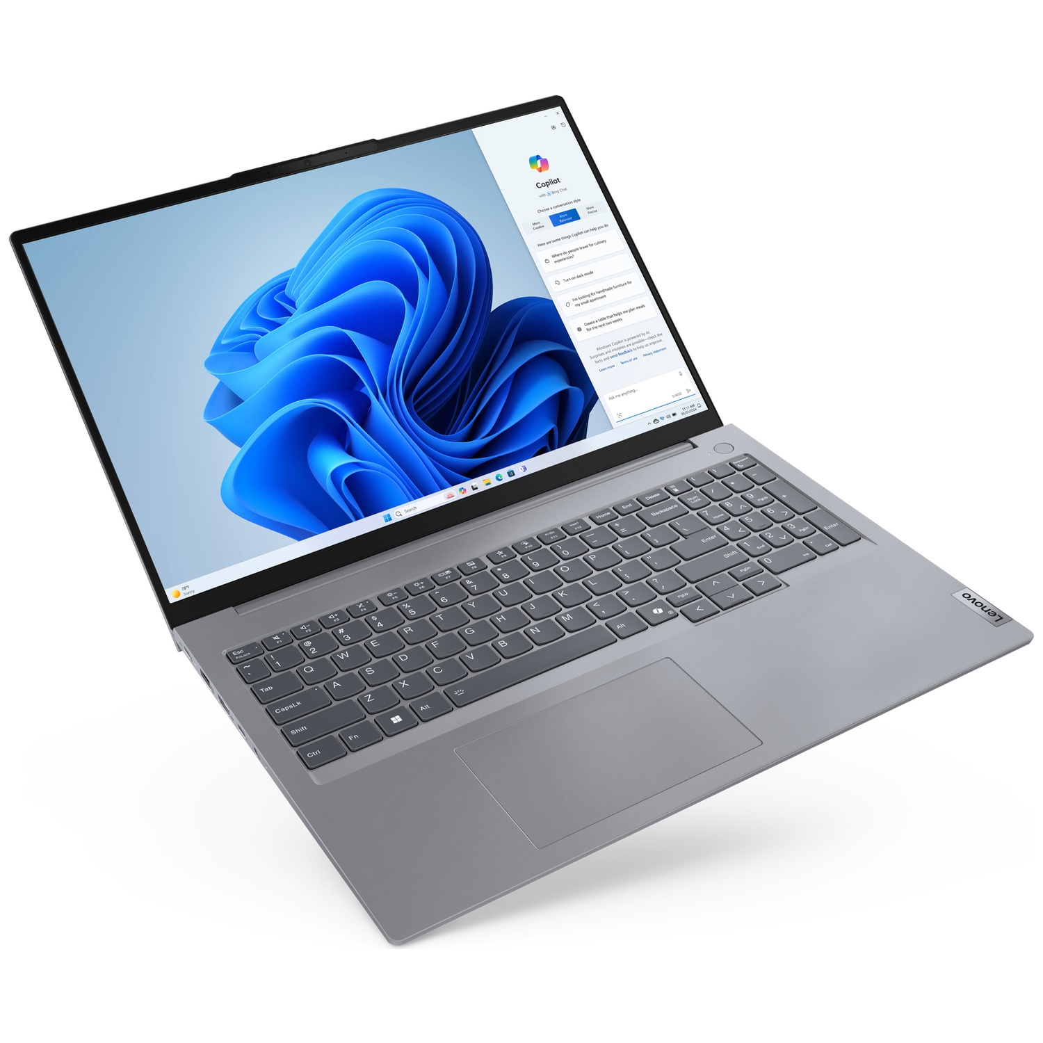 Un ordinateur portable Lenovo gris affichant un fond Windows 11 bleu abstrait. L'écran affiche l'interface Copilot.