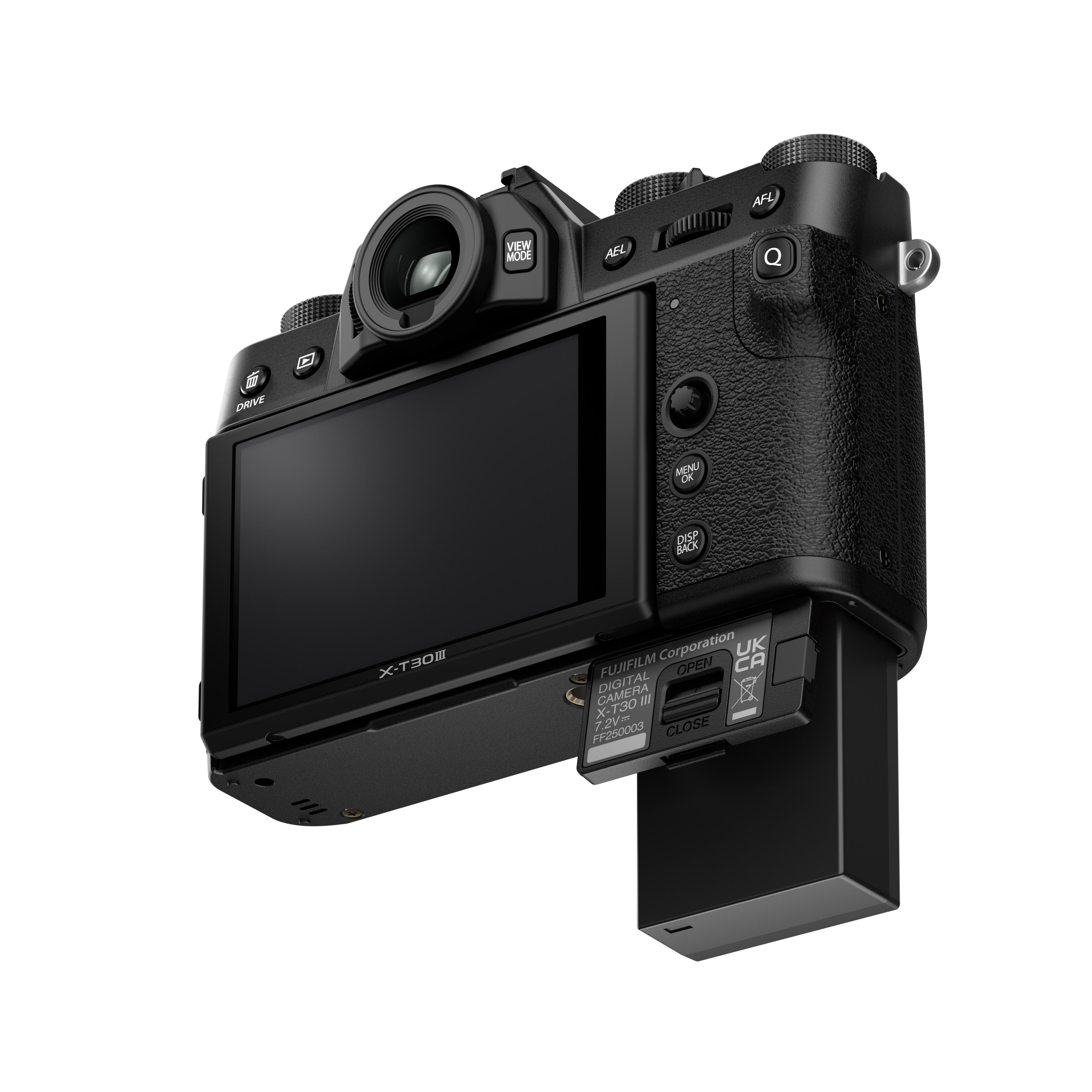 Schwarze Fujifilm X-T30 III Kamera, abgewinkelt, mit sichtbarem Bildschirm, geöffnetem Akkufach und weißem Hintergrund.