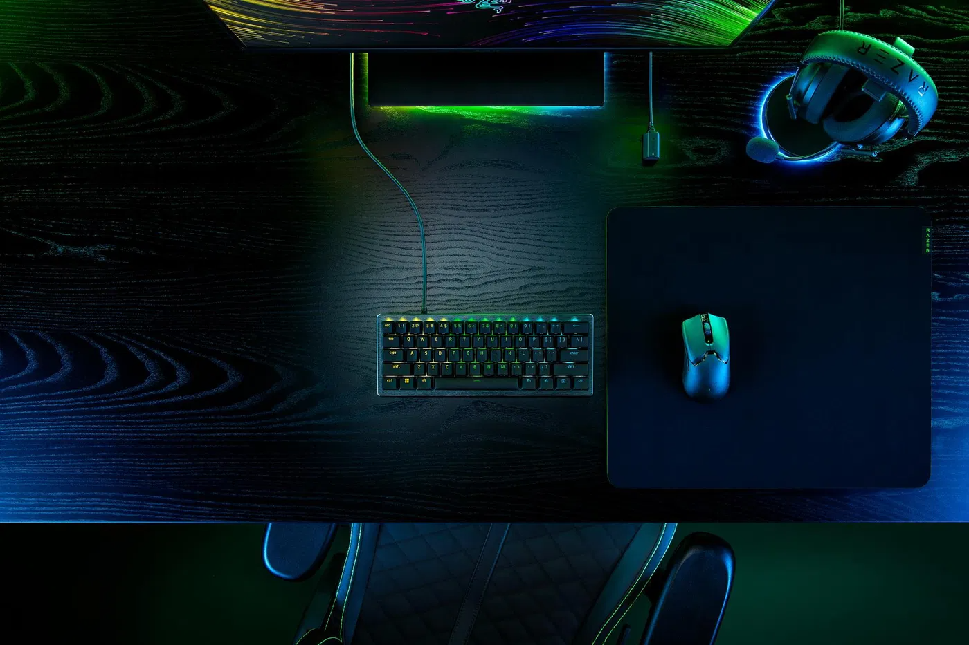 Játékbeállítás. Billentyűzet, egér, fejhallgató és monitor sötét faasztalon. Az RGB világítás hangsúlyozza a jelenetet.