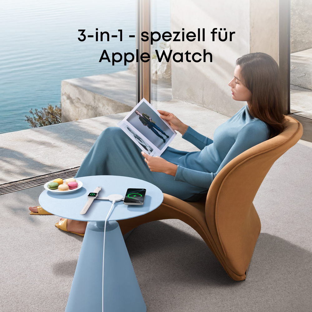 Frau liest Magazin, sitzt in Stuhl neben Tisch mit Uhr, Telefon und Makronen. Meer im Hintergrund sichtbar.