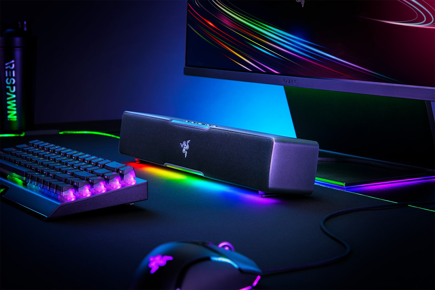 Játékbeállítás billentyűzettel, egérrel, hangszóróval és monitorral. Mind RGB világítással. Fekete asztal és sötét háttér.