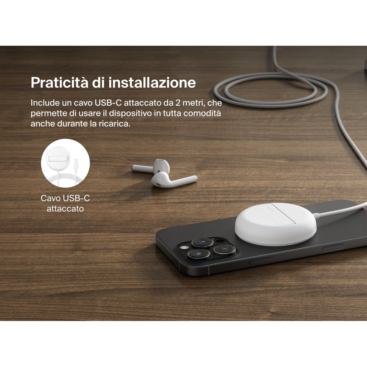 Un pad di ricarica bianco è su un telefono nero. Auricolari bianchi e un cavo USB-C sono anche su legno.