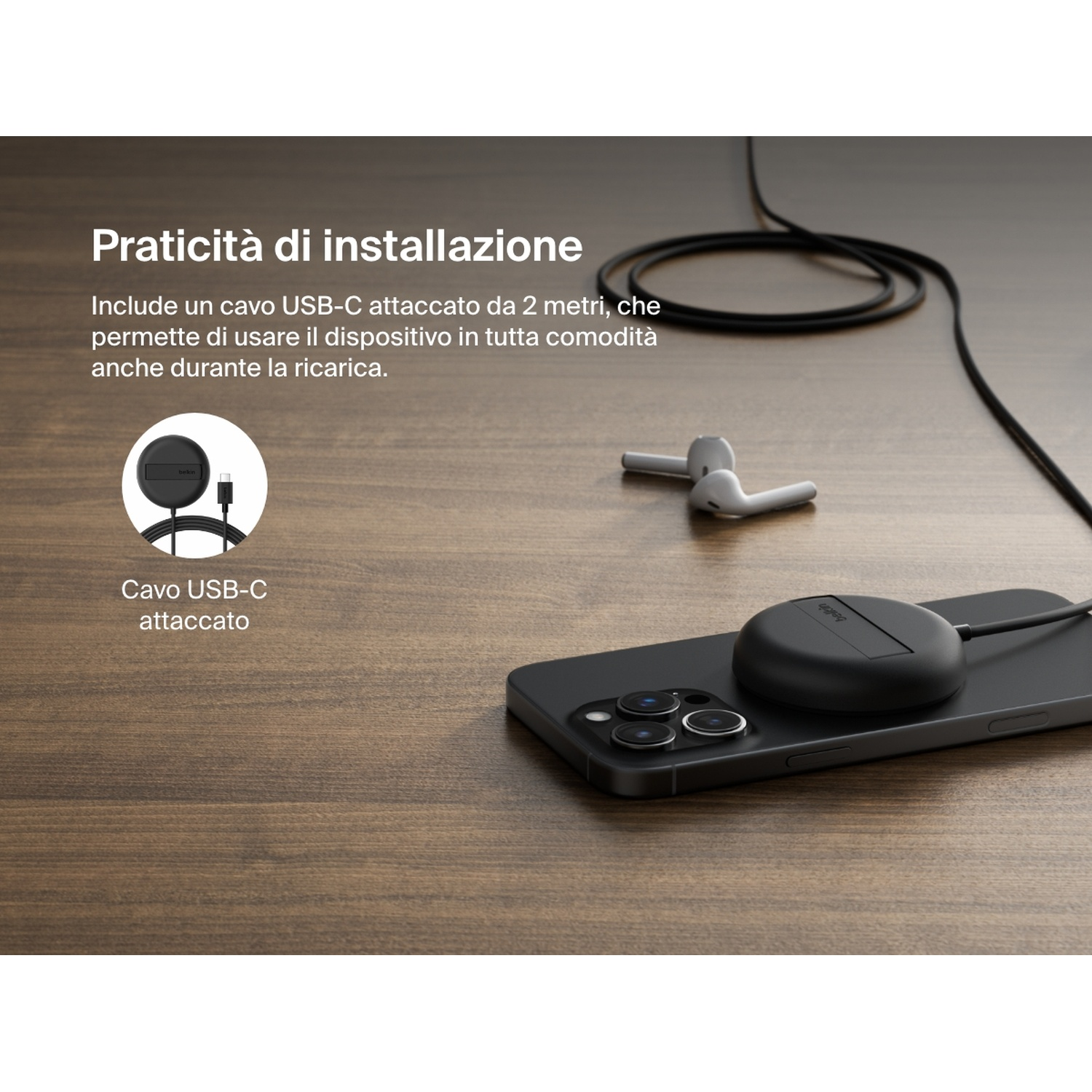 Un telefono nero con un caricatore wireless nero su una superficie di legno. Auricolari bianchi sulla superficie. Un cavo USB-C è collegato.