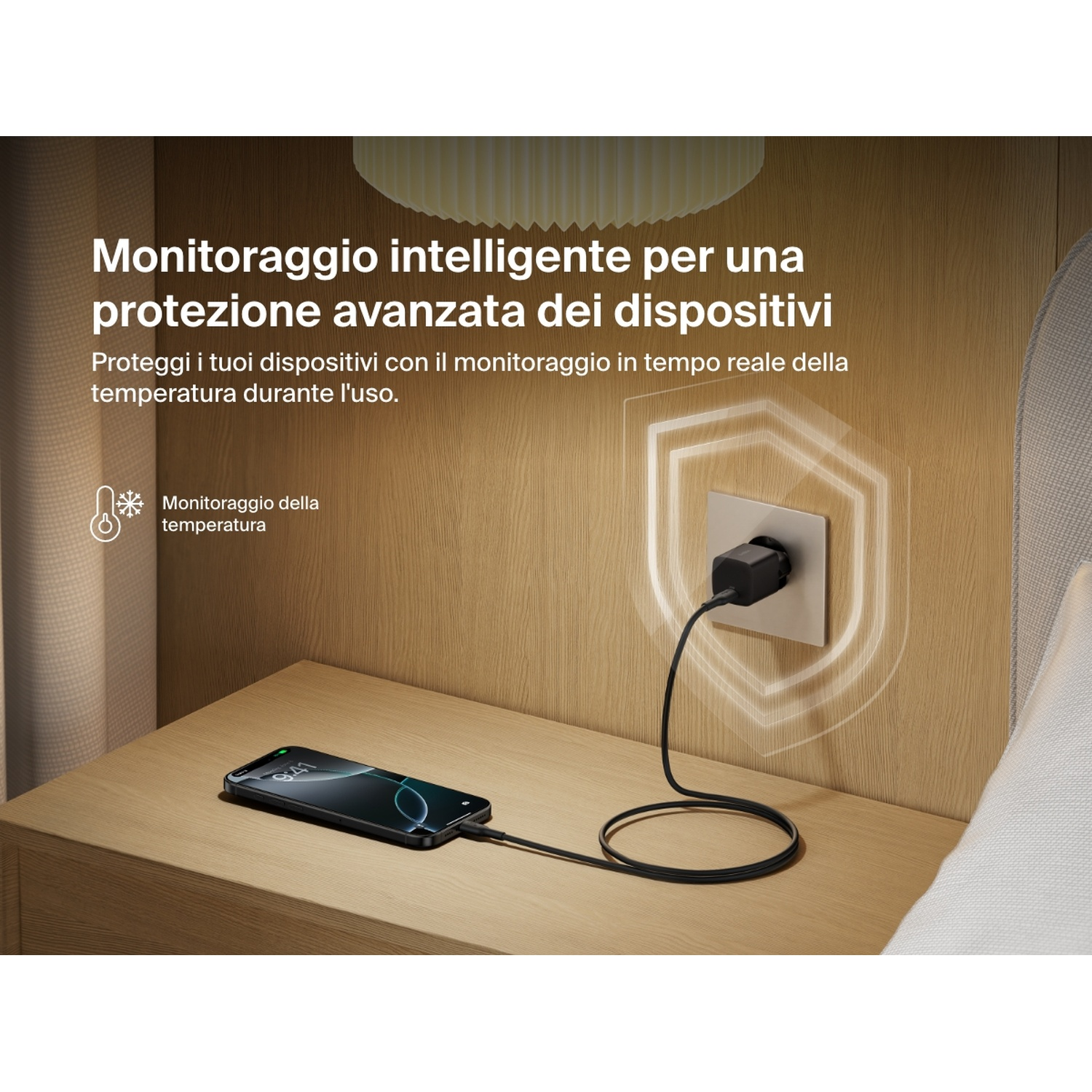Un telefono si carica su un comodino di legno. Un caricabatterie nero è collegato alla parete. Testo in italiano visibile.