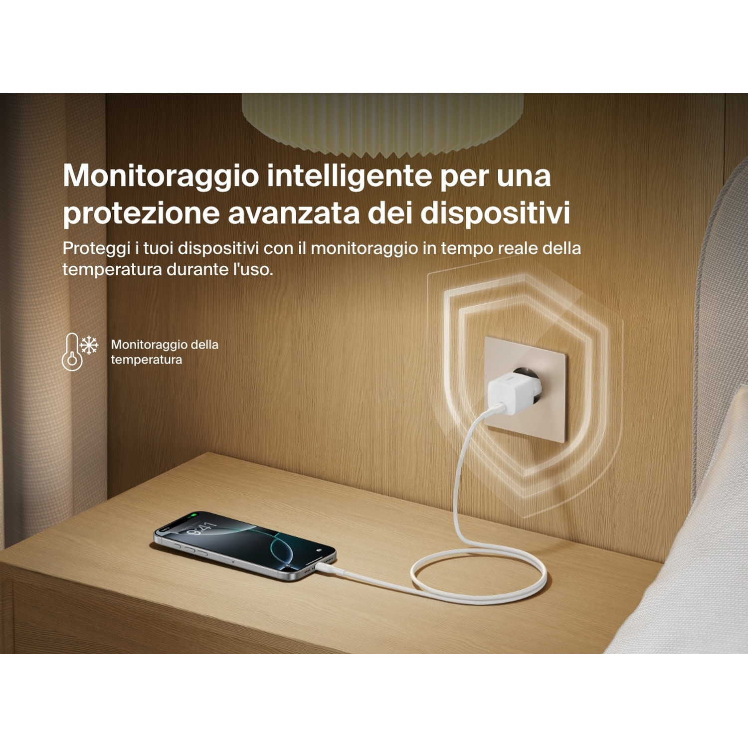 Un telefono si carica su un comodino. Una presa a muro con un caricabatterie bianco. Il testo descrive il monitoraggio intelligente per la protezione del dispositivo.