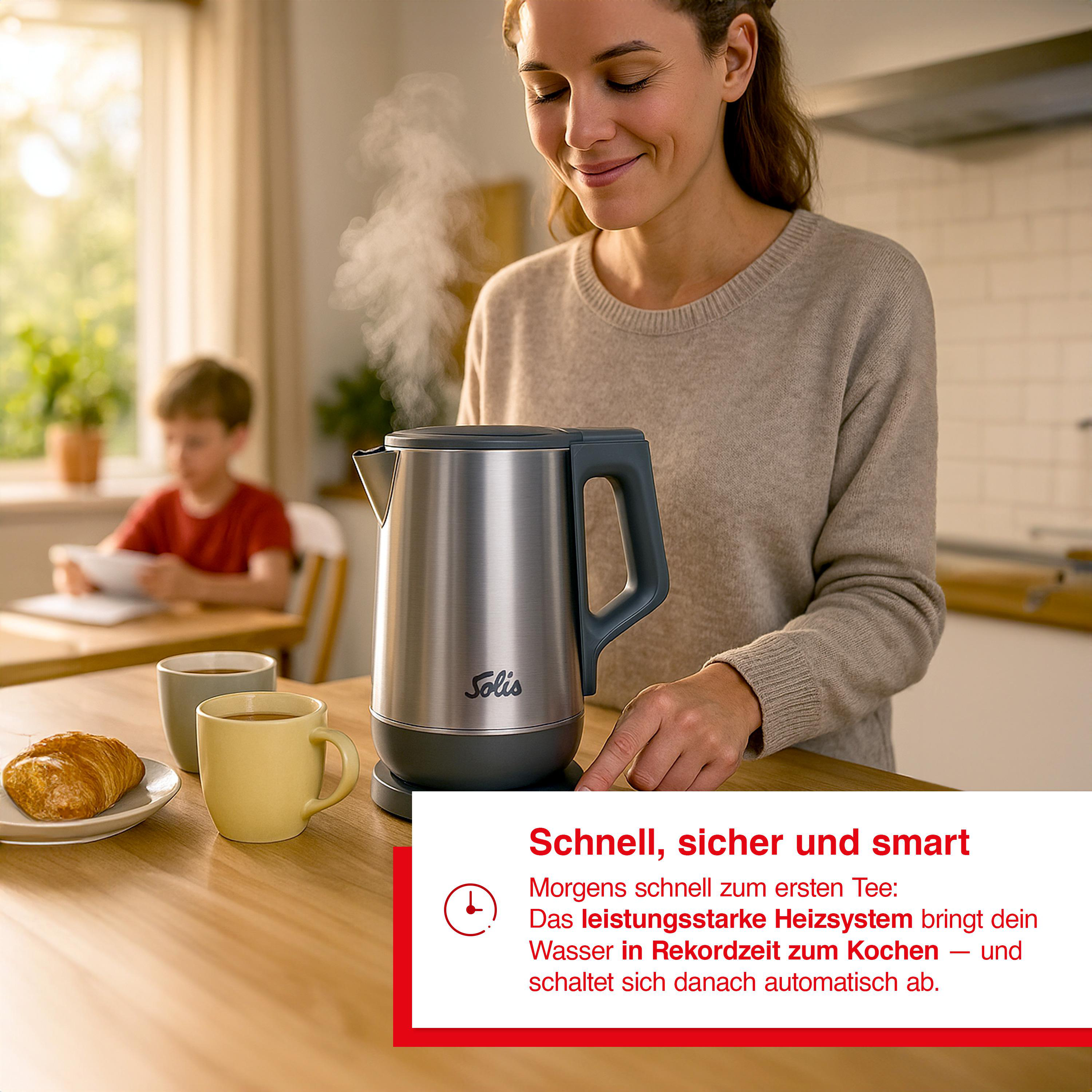 Eine Frau lächelt neben einem Wasserkocher. Dampf steigt auf. Ein Kind und Tassen sind im Hintergrund. Ein Croissant liegt auf einem Teller.