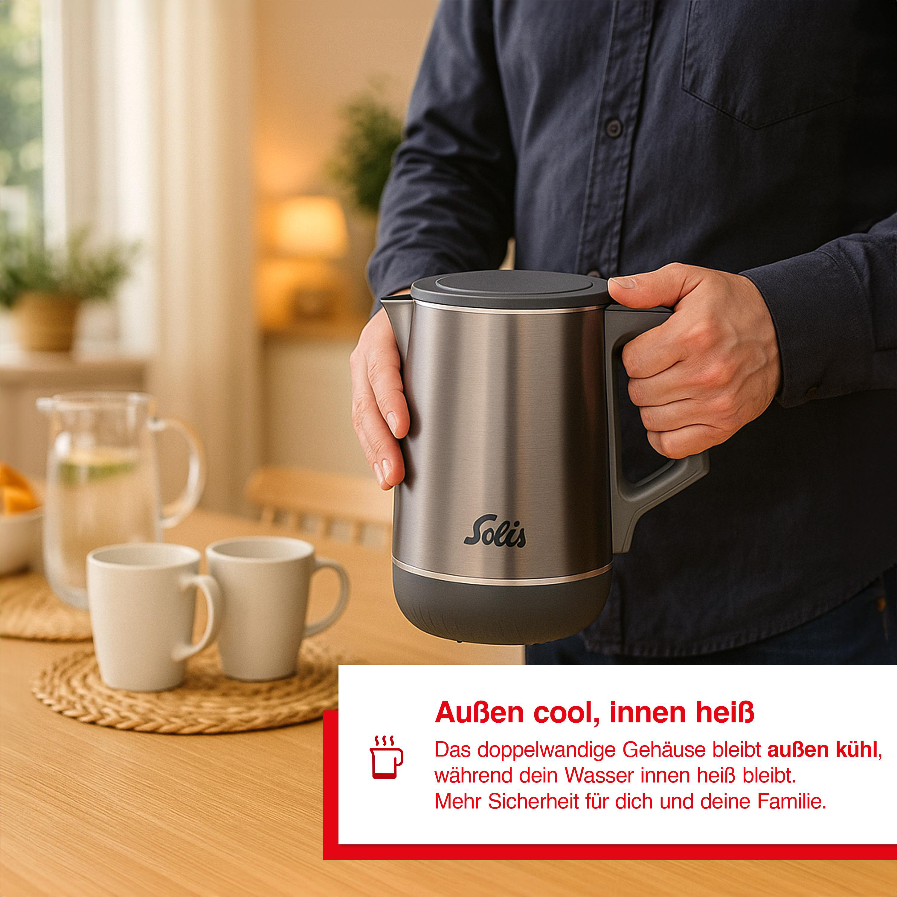 Eine Person hält einen silbernen Solis-Wasserkocher. Zwei weiße Tassen und eine Wasserkaraffe stehen auf einem Tisch. Text: Außen cool, innen heiß.